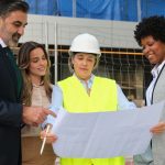 Team of architects and engineers reviewing blueprints on construction site